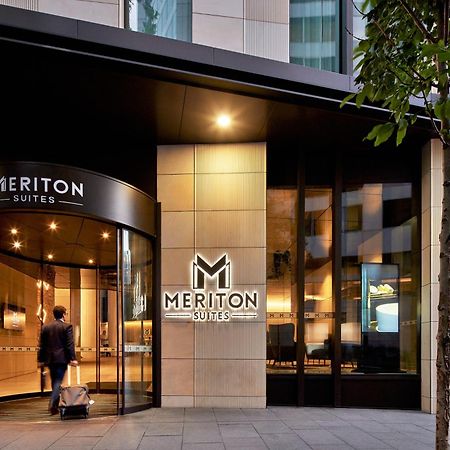 Meriton Suites Sussex Street, Сидни Екстериор снимка The photo shows the entrance of a hotel or suite establishment named "Meriton Suites." The entrance features a revolving door and a large, illuminated sign with the name "MERITON SUITES." The facade is modern and sleek, with a combination of glass an