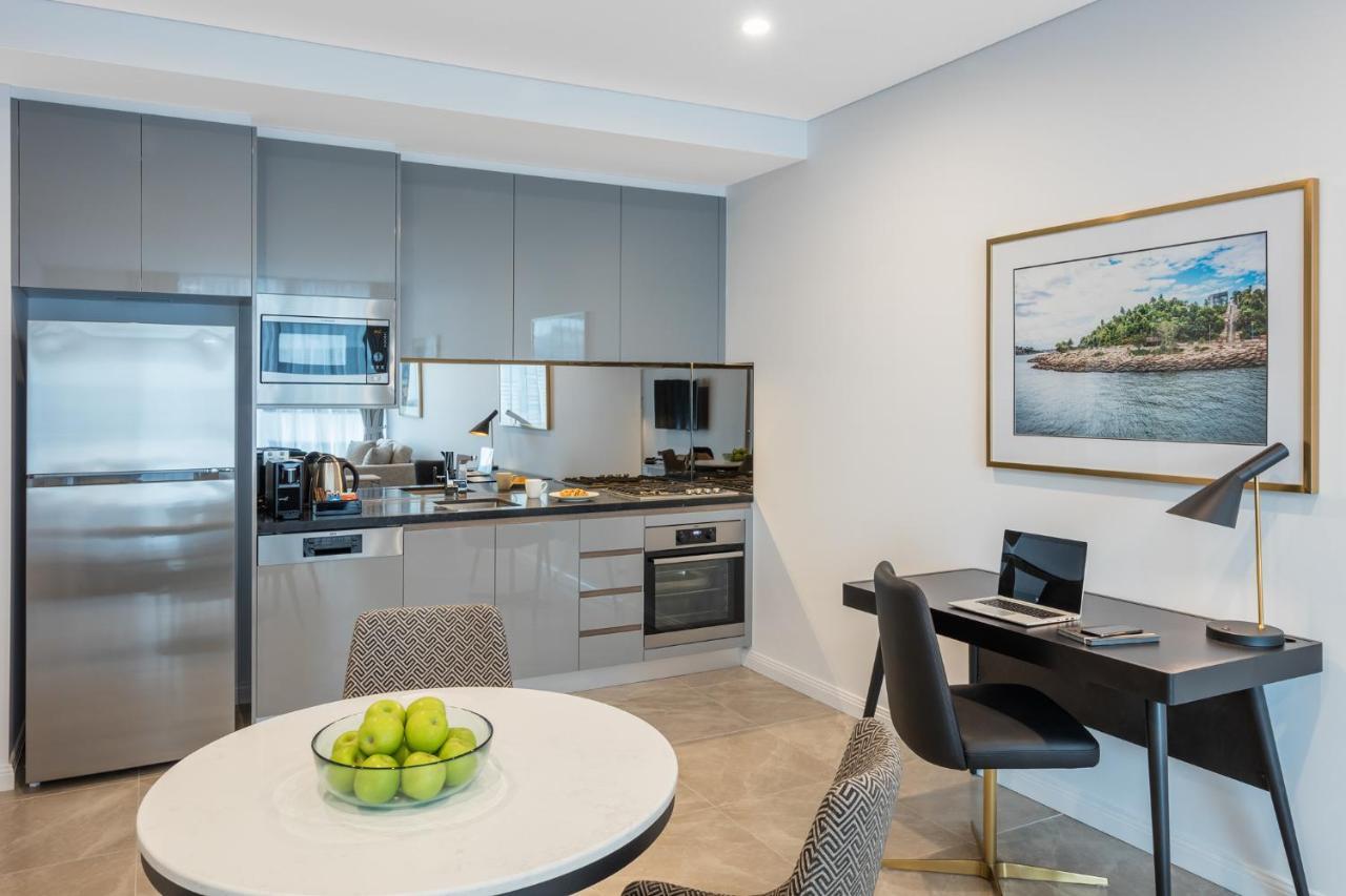 Meriton Suites Sussex Street, Сидни Екстериор снимка The photo shows a modern kitchen and dining area in an apartment. The kitchen features sleek gray cabinetry, a stainless steel fridge, and a microwave. There is a countertop with cooking appliances, including an oven and stovetop. A small round dinin