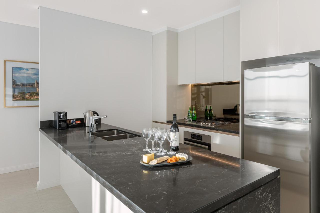 Meriton Suites Sussex Street, Сидни Екстериор снимка The photo shows a modern kitchen featuring a sleek design with a dark stone countertop. There is a built-in sink and possibly a cooktop. The kitchen cabinetry is light-colored, creating a contrast with the dark counter. On the countertop, there are w