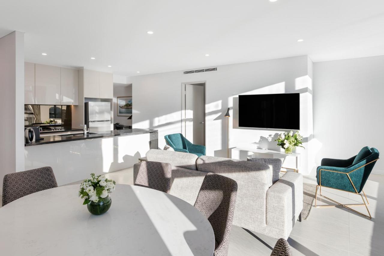 Meriton Suites Sussex Street, Сидни Екстериор снимка The photo shows a modern, bright living space that combines a kitchen and a living area. The kitchen features sleek cabinets and stainless steel appliances. In the foreground, there is a round dining table with a vase of flowers on it. Seating option