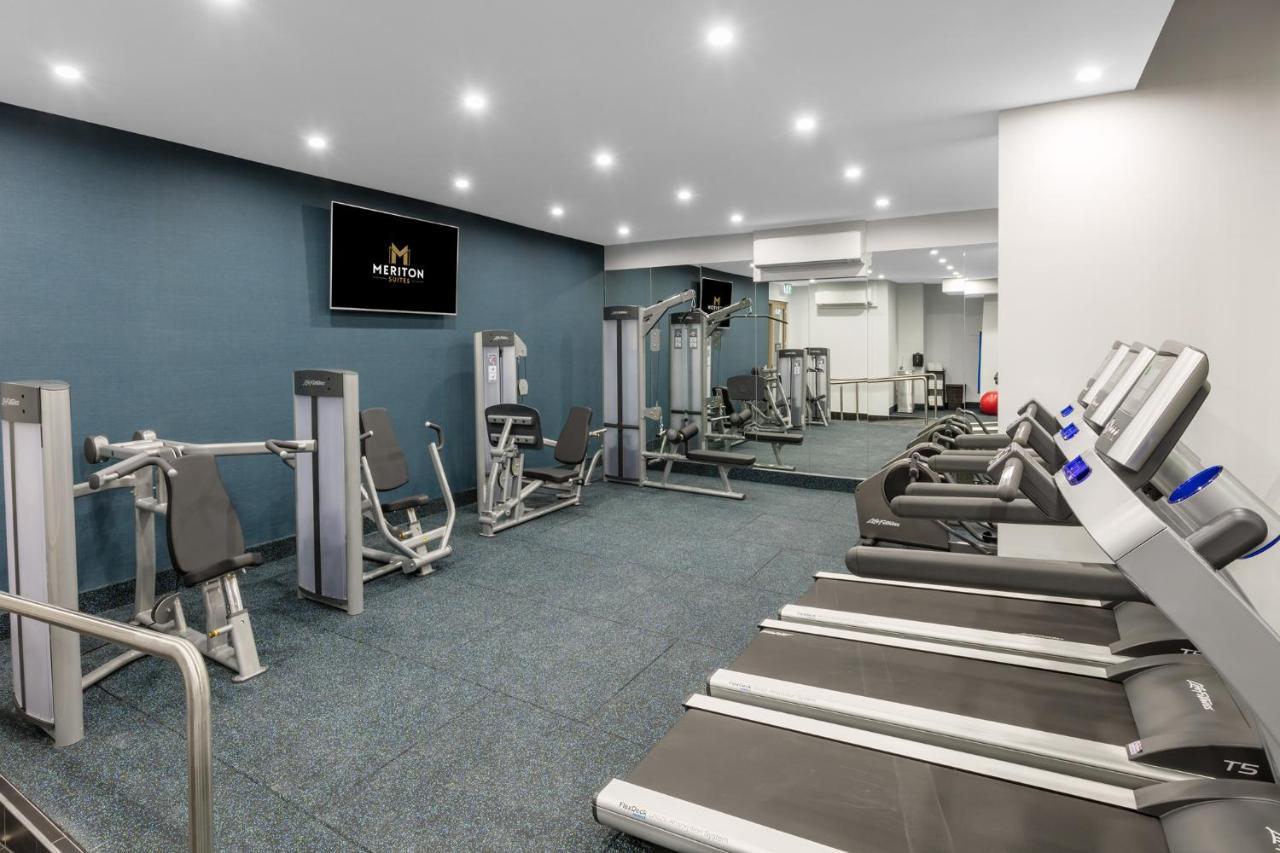 Meriton Suites Sussex Street, Сидни Екстериор снимка The photo shows a modern gym interior. The space features several pieces of exercise equipment, including weight machines and stationary bikes. The walls are painted a calming color, and the flooring is carpeted. There are also mirrors on the walls, 
