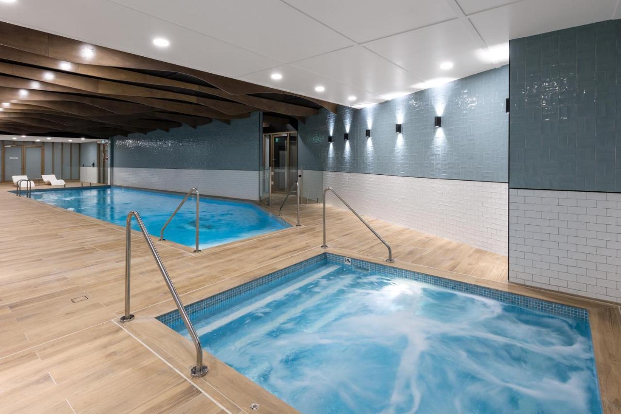 Meriton Suites Sussex Street, Сидни Екстериор снимка The photo shows a modern indoor spa area. There are two pools: one is larger and has a clear blue water, while the other is smaller, possibly a hot tub, with jets creating bubbles. The walls are a mix of blue tiles and white tiles, and the floor is m