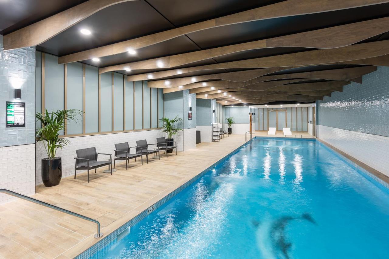 Meriton Suites Sussex Street, Сидни Екстериор снимка The photo shows an indoor swimming pool area. The pool has clear blue water and is flanked by a wooden deck. There are several lounge chairs arranged along one side of the pool. The ceiling features a modern design with wooden beams and recessed ligh