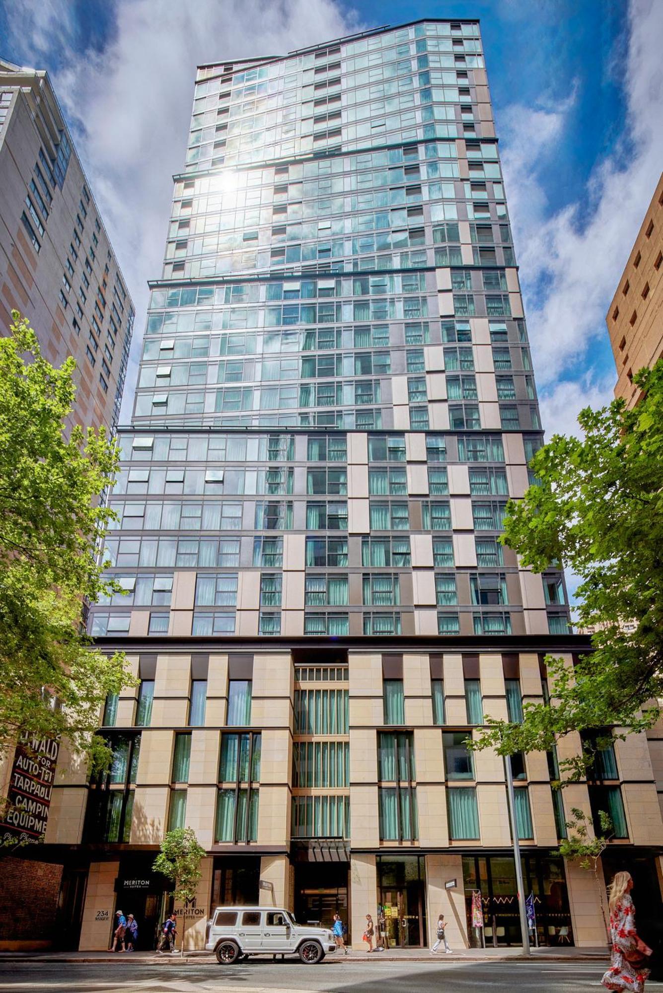 Meriton Suites Sussex Street, Сидни Екстериор снимка The photo shows a tall modern building with a glass facade and various architectural design elements. The structure has multiple stories, with large windows that reflect the surrounding environment. At the base, there are sections that appear to have