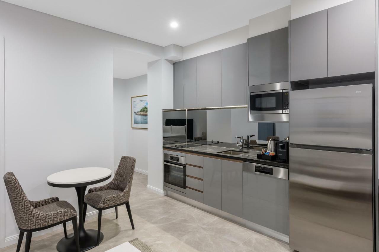 Meriton Suites Sussex Street, Сидни Екстериор снимка The photo shows a modern kitchen area that features a sleek design. The cabinetry and appliances are in shades of gray, giving it a contemporary look. There is a stainless steel refrigerator, microwave, and oven, along with a sink and cooking area. 
